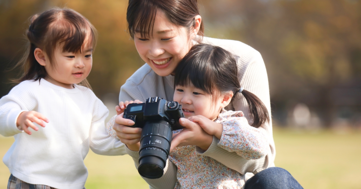 母親に寄り添いながら、大きなカメラの画面を楽しそうに見つめる2人の女の子