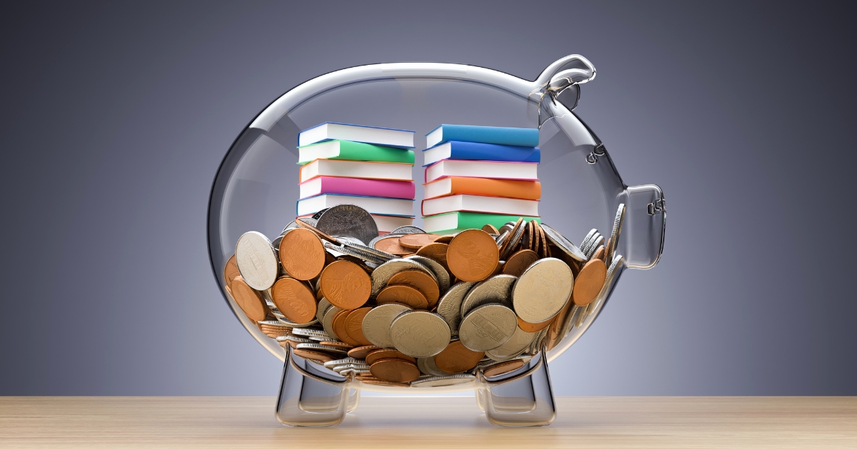 カラフルな本が入った透明な豚の貯金箱。子どものお金教育・貯金習慣のイメージ