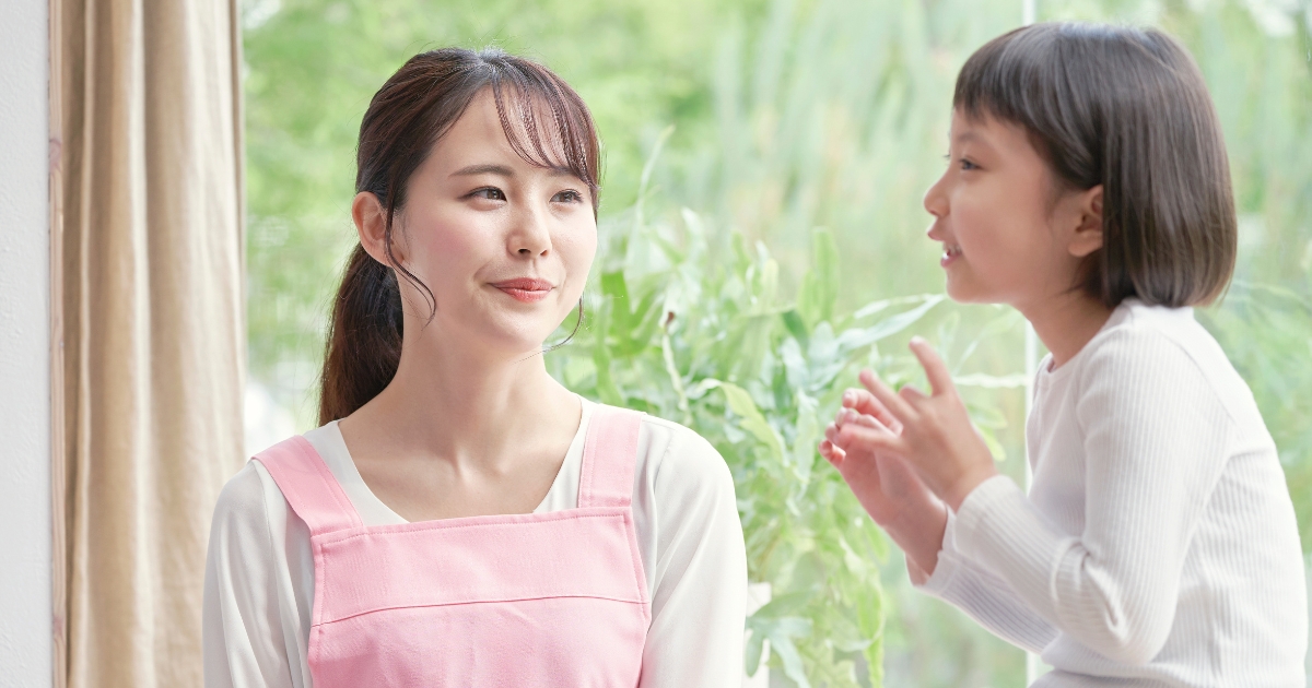 ピンクのエプロンを着た先生に、笑顔で楽しそうに話しかける女の子の様子