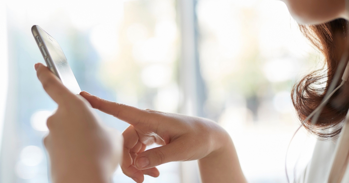 スマートフォンの画面を指で操作する女性の手元。子どものスマホ課金・キャッシュレス決済のイメージ