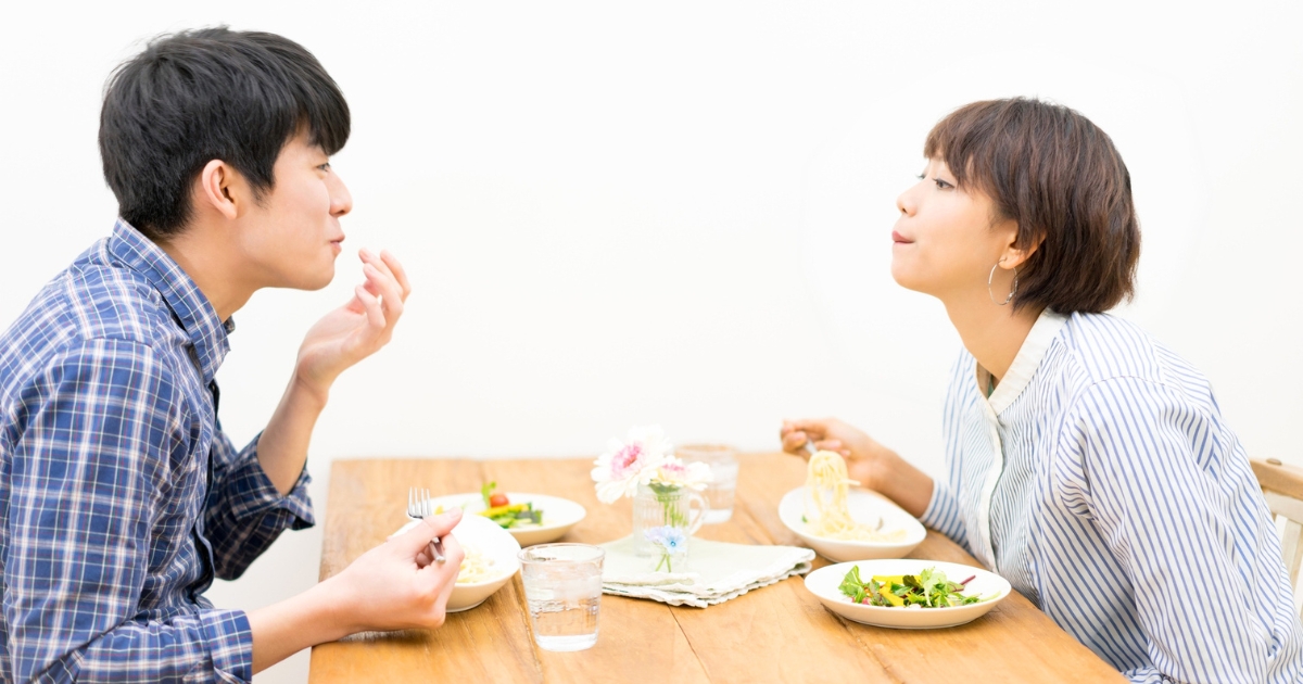 白い背景の食卓で、向かい合って食事を楽しむ夫婦