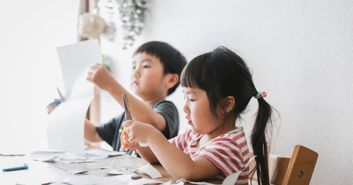 室内ではさみを使って紙を切り、工作に集中している子どもたち。体験学習・創造力のイメージ