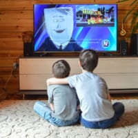 リビングでテレビを並んで見ている2人の子ども。兄が弟の肩に腕を回している