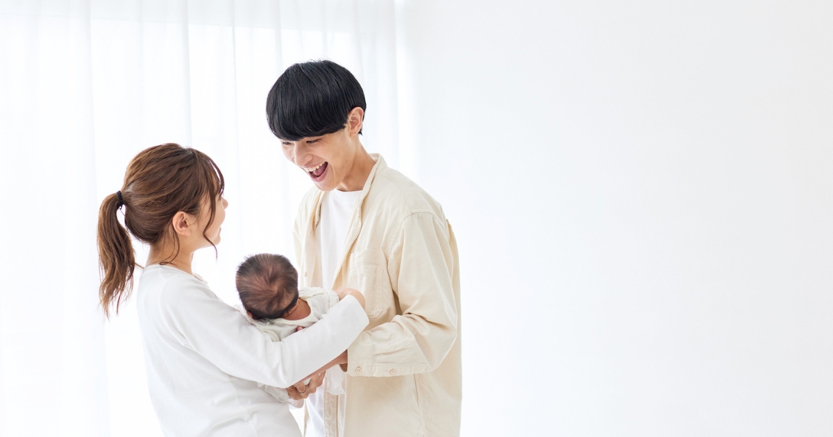 赤ちゃんを抱っこする妻に寄り添い、愛おしそうに笑顔を向ける父親の姿