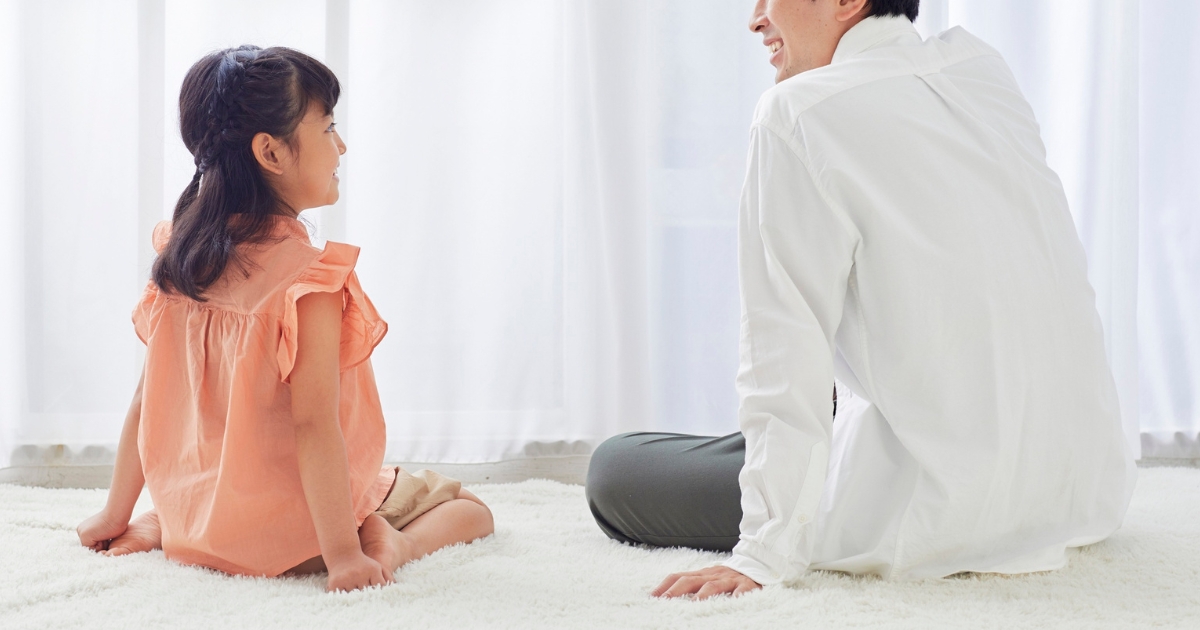 床に座って向き合い、笑顔で話す父親と娘