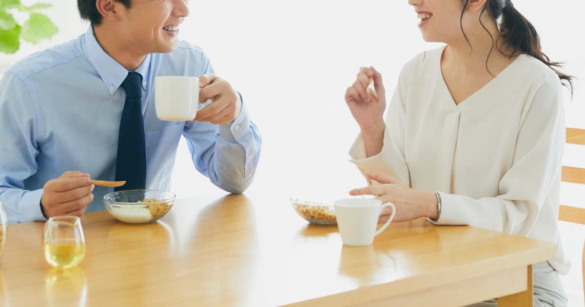 朝食のテーブルで、向き合って笑顔で話す夫婦