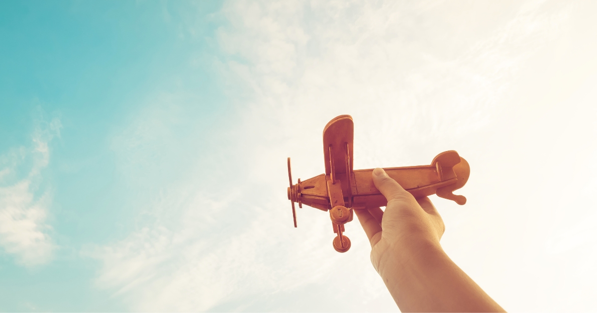 どもの手が、青空に向かって木製のおもちゃの飛行機を高くかかげている