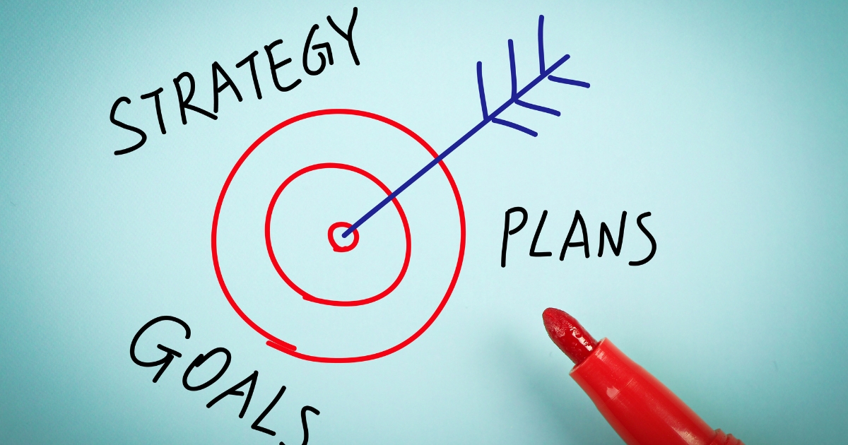 青い矢印が中心に命中した赤い的の周りに、「STRATEGY」「PLANS」「GOALS」と手書きされ、右下に赤いマーカーペンが置かれている
