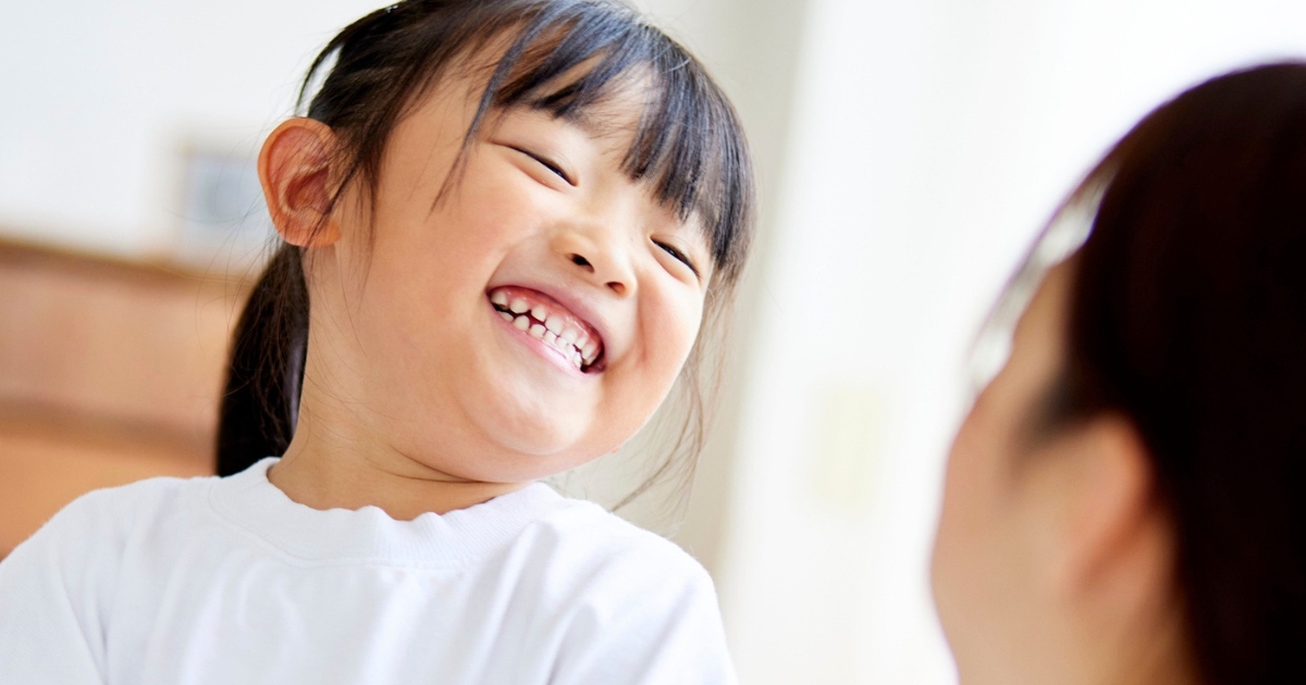 笑顔で大きく笑う女の子が、向かいにいる大人に楽しそうに話しかけている様子