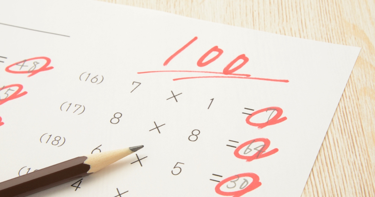 木製テーブルの上に置かれた、赤ペンで採点されたテスト用紙。大きく「100」と書かれ、丸がついている。手前に鉛筆がある