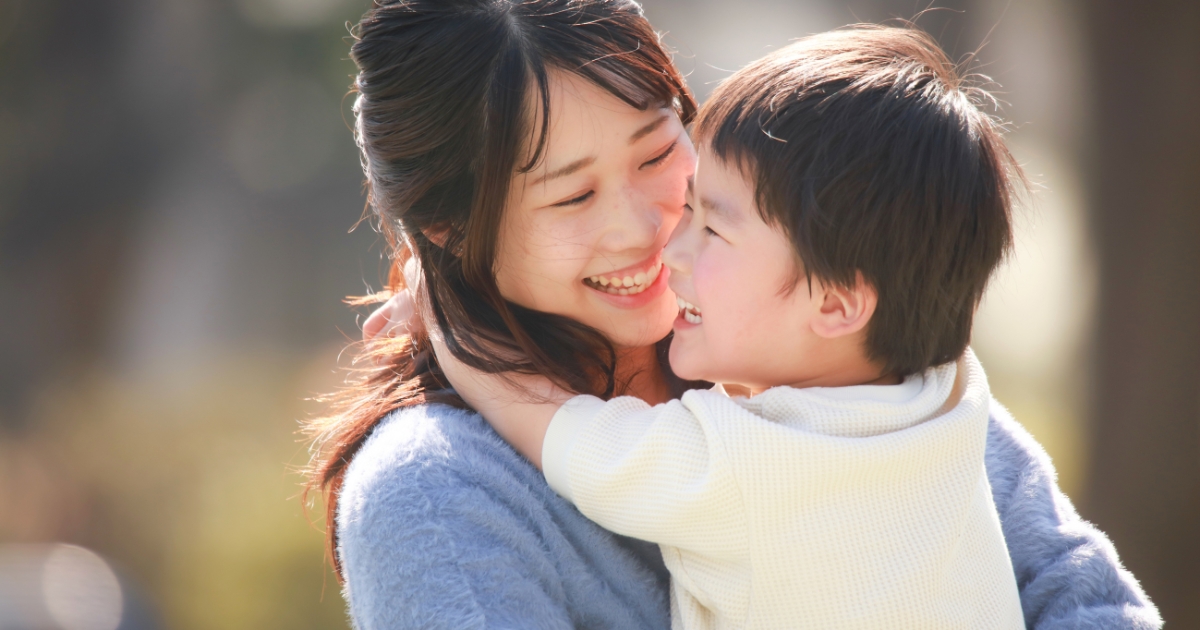 明るい日差しの中、満面の笑みで顔を寄せ合い、しっかりと抱きしめ合う母親と男の子
