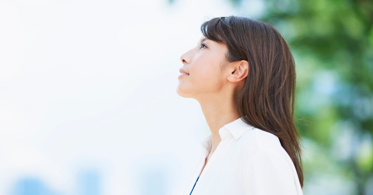 穏やかな表情で上を見上げる、白いシャツを着た女性の横顔
