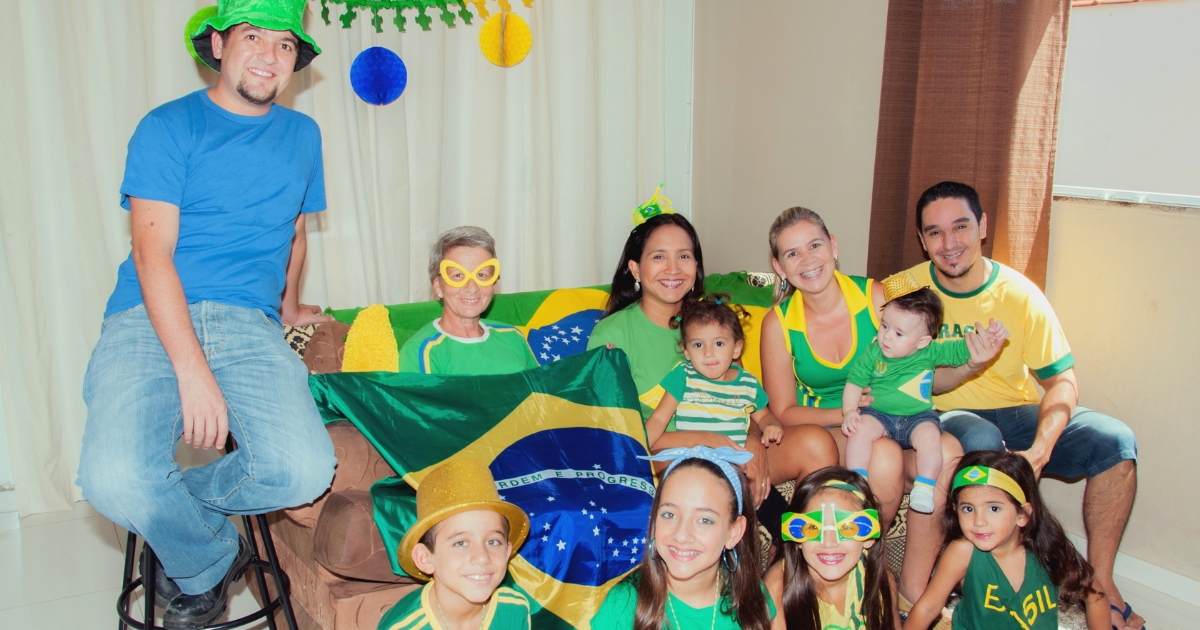 ブラジル国旗や黄色と緑の服、応援グッズを身につけ、室内で笑顔で集まっている家族や友人たちのグループ