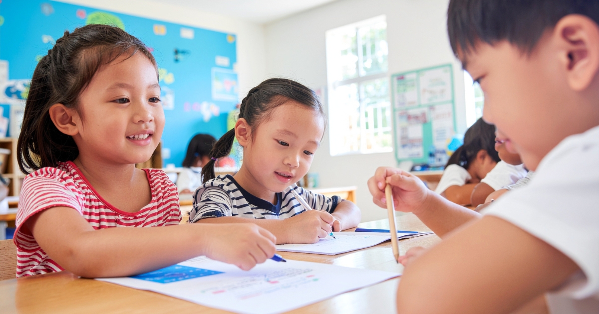 机に向かって一緒に書き物をしている3人の子どもたち