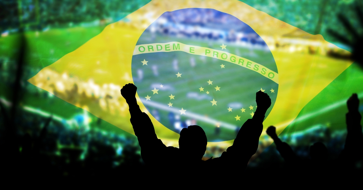 ブラジル国旗が透けて重なる、スタジアムで両手を挙げて歓声を上げるサポーターのシルエット