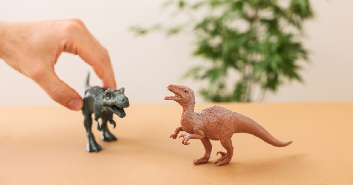 机の上に置かれた2体の恐竜のフィギュアを使い、手を伸ばしてごっこ遊びに参加している様子