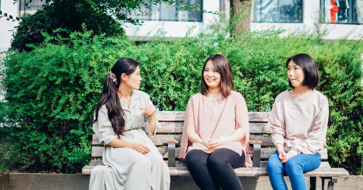 ママ友3人がベンチに座って会話する様子