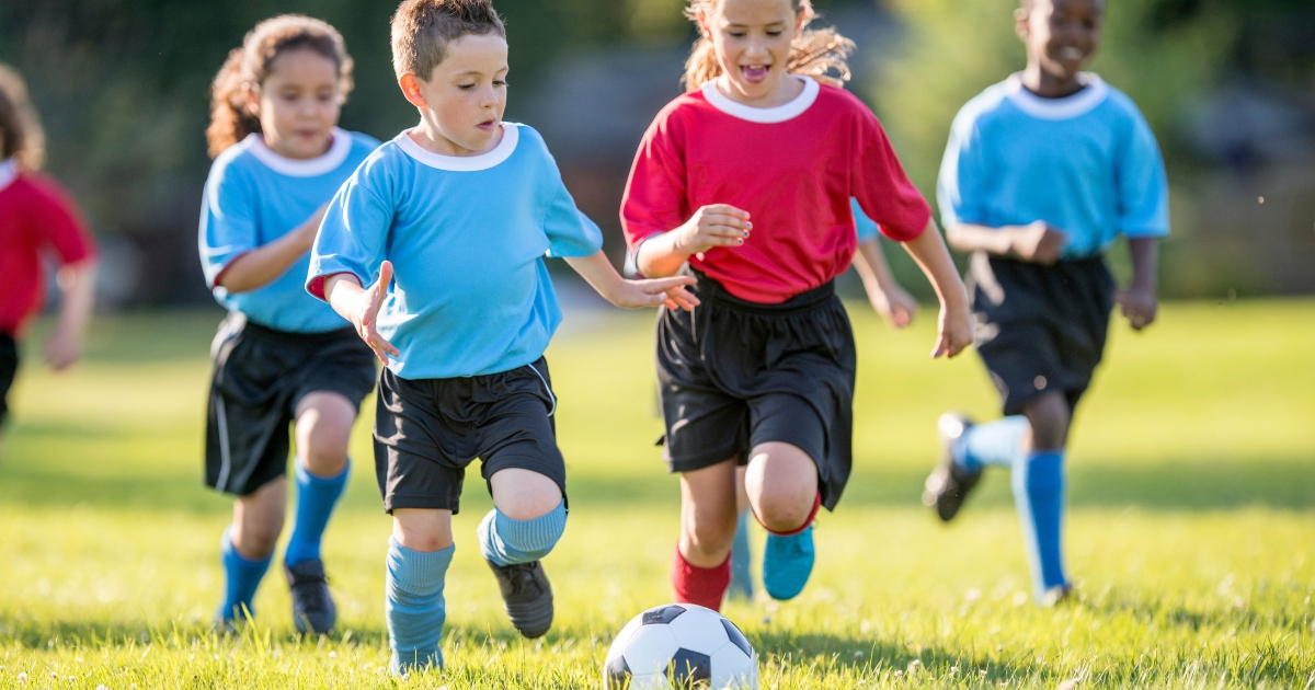 晴れた日の芝生の上で、楽しそうにサッカーボールを追いかけて走るユニフォーム姿の子どもたち