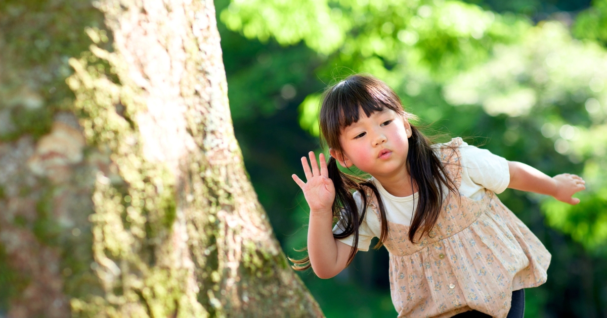 森の中で大きな木のそばに立ち、耳に手を当てて自然の音を聴こうとしている女の子