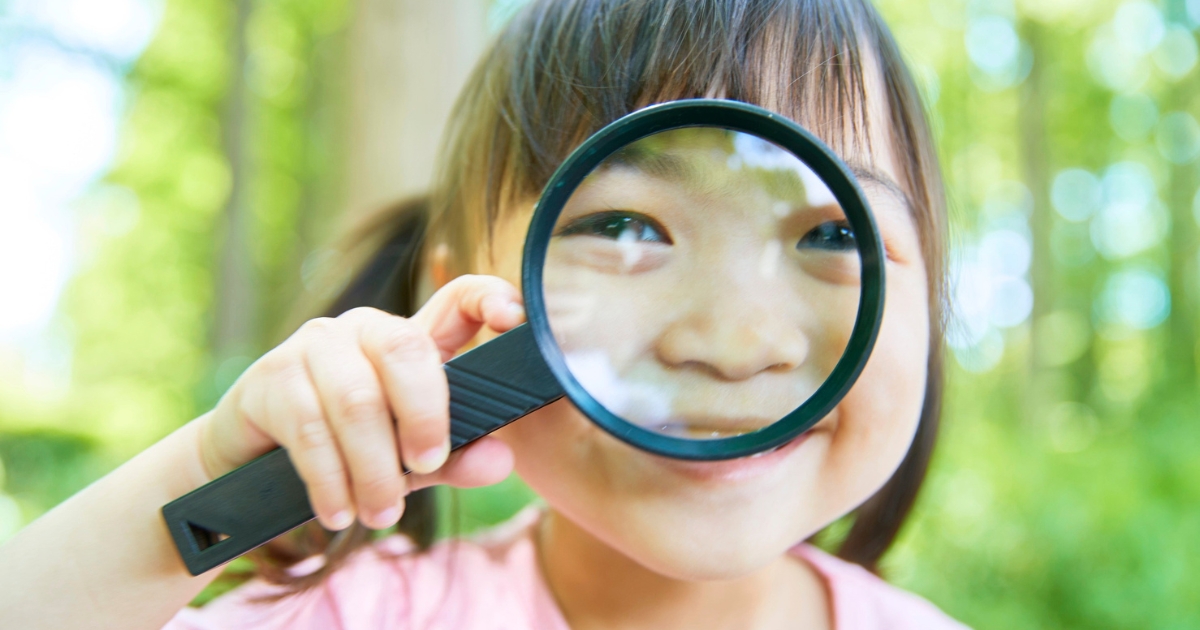 森の中で虫眼鏡を覗き込み、笑顔を見せる小さな女の子