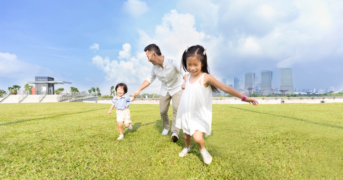 芝生の上でパパとこどもふたりがてをつないで走る様子