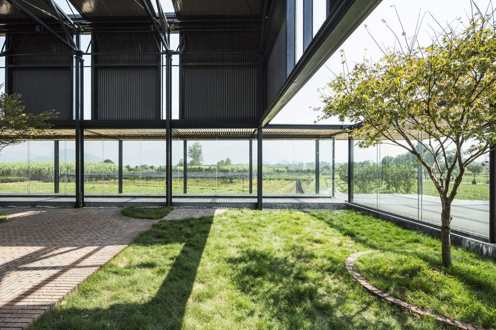 Grass and brick paths inside a tall glazed pavilion