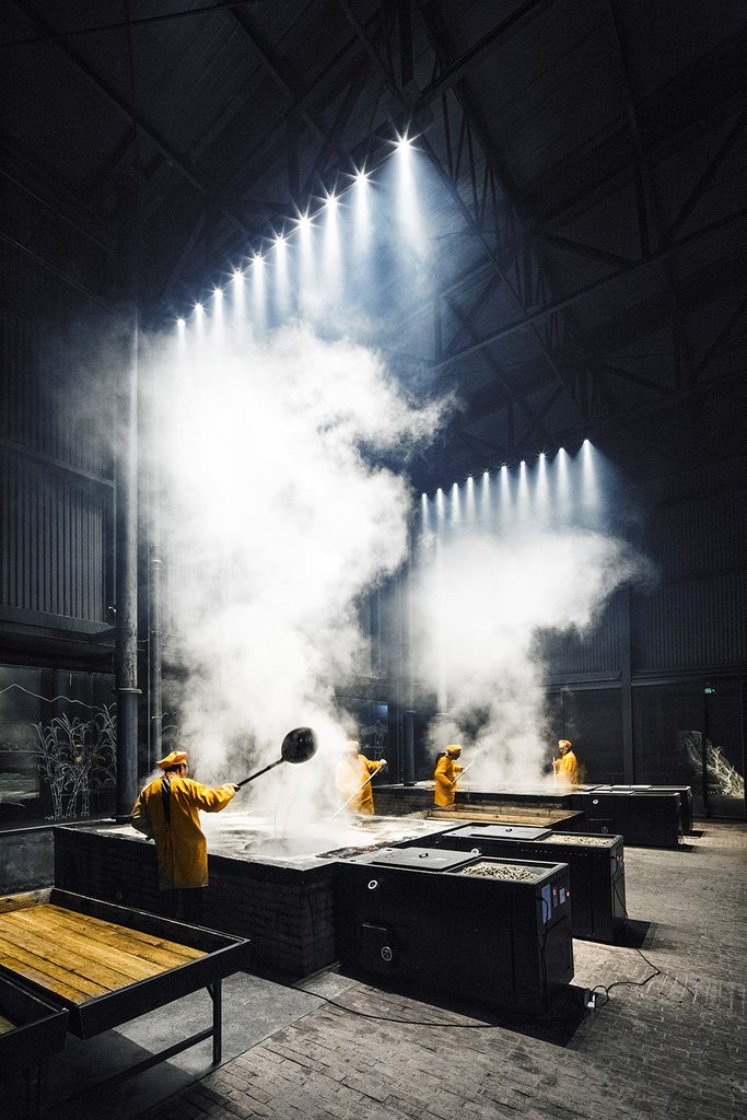 Worker tending a steaming pot beneath a rooflight