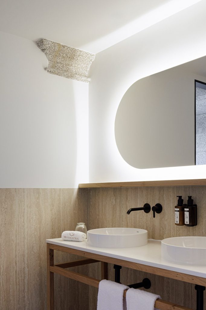 Twin basins beneath a backlit mirror beside historic stonework