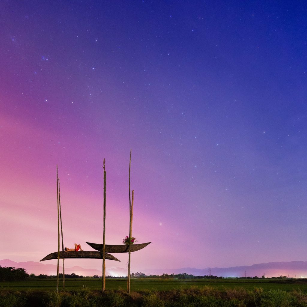 A figure resting on a boat under a purple dusk sky