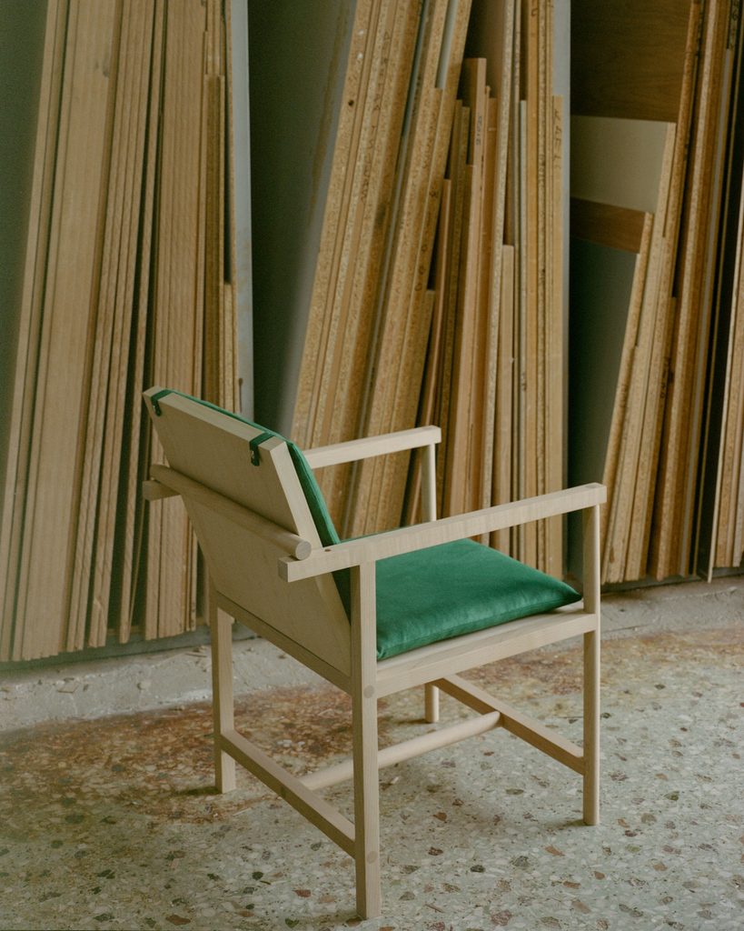 Parrot Chair beside stacked timber boards inside a workshop.