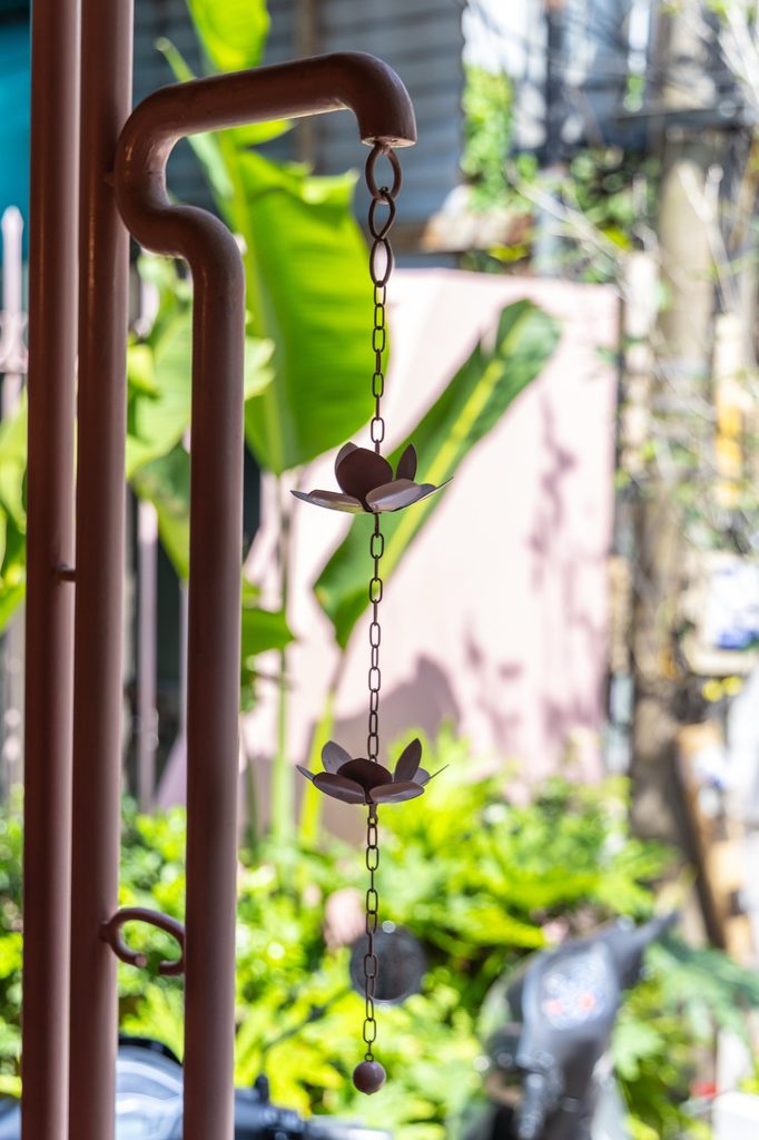 Close view of a metal rain chain beside green foliage