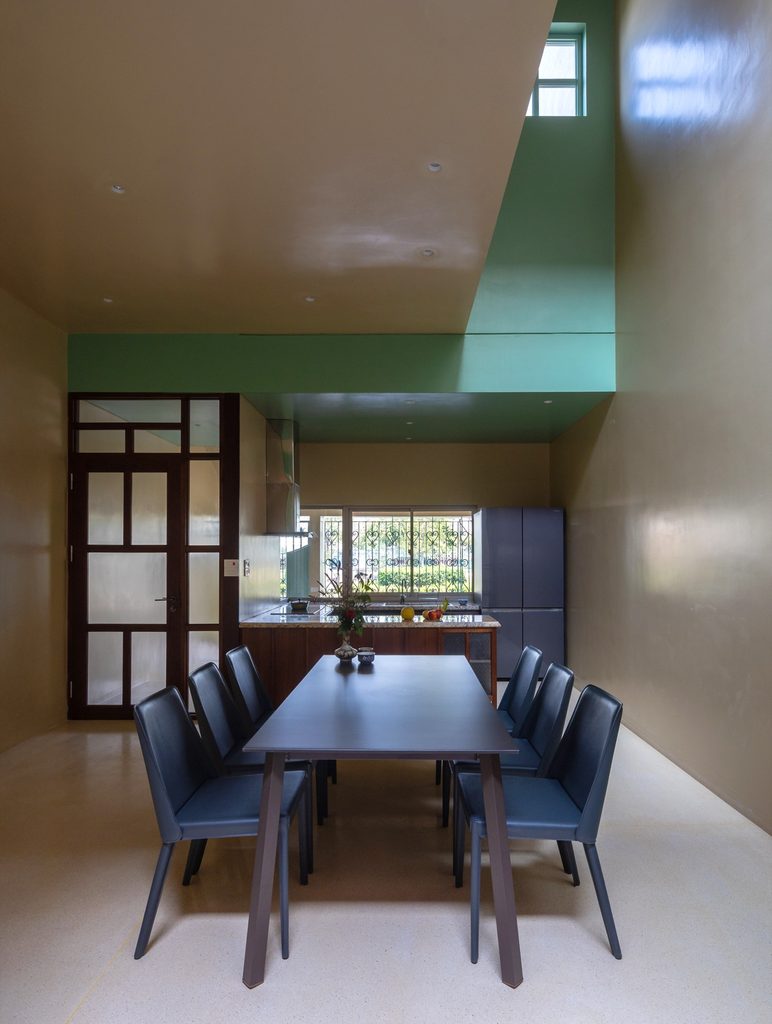 Dining table beneath a tall ceiling with the kitchen beyond