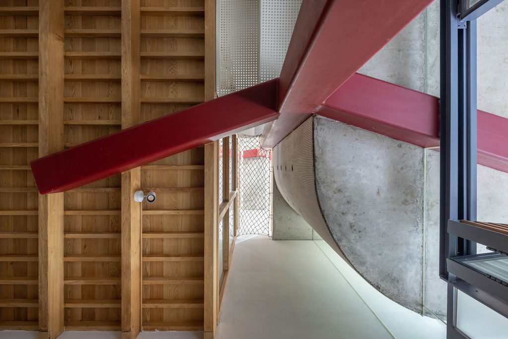 Red steel beam beneath timber slats beside a curved concrete slab