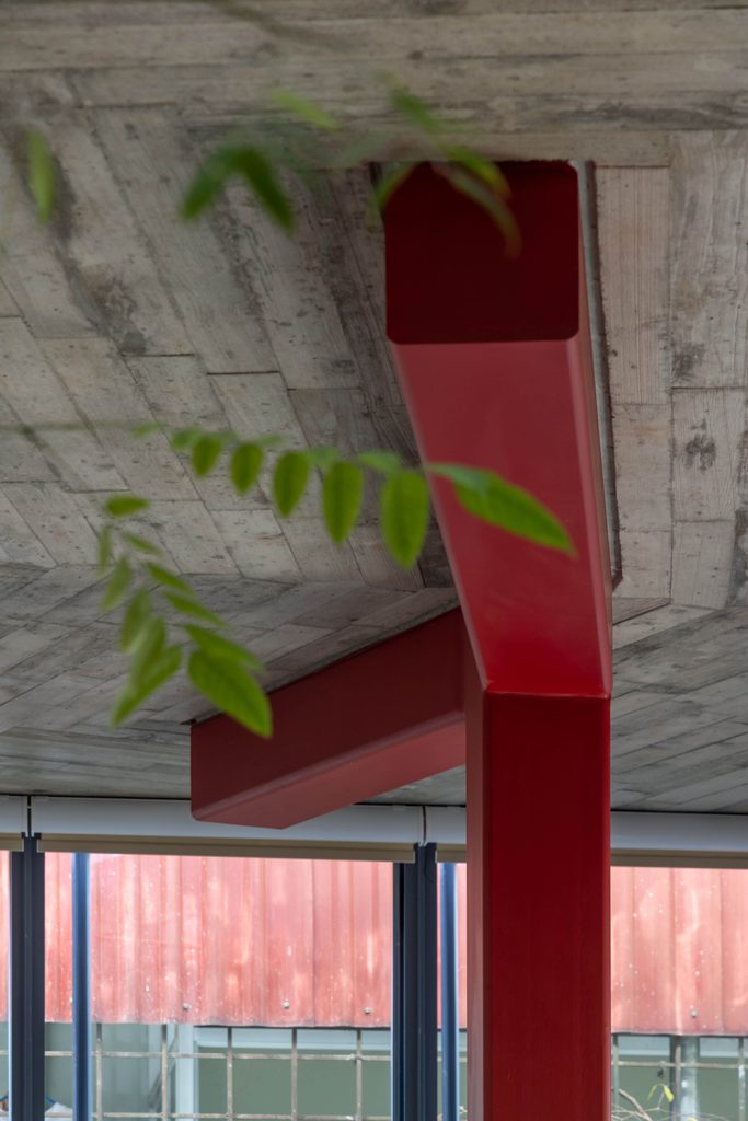 Red steel column and beam beneath an exposed concrete ceiling