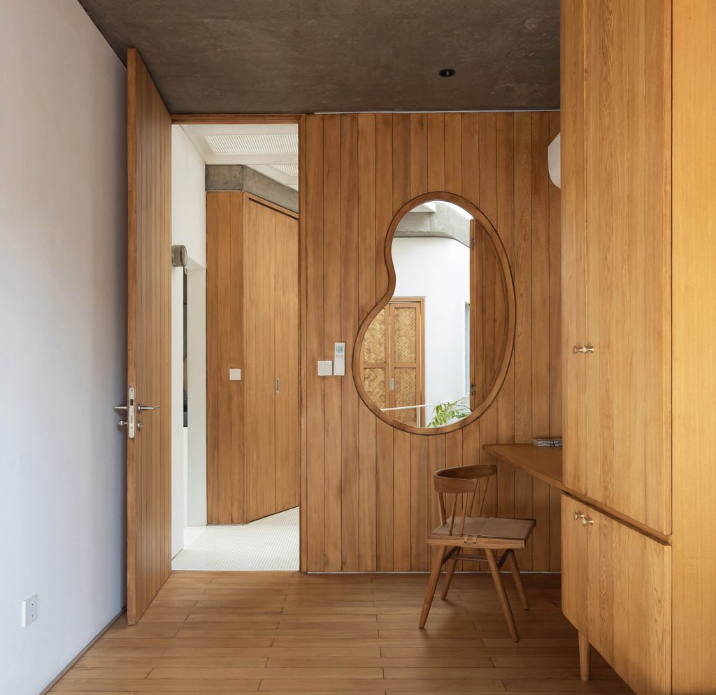 Timber cabinetry and a curved mirror beside the bathroom