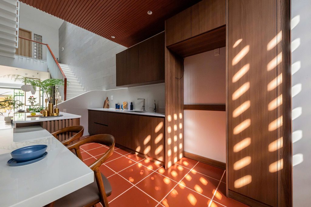 Kitchen cabinetry and red floor tiles patterned by sunlight
