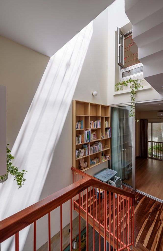 Sunlight reaches an upper landing with a timber bookshelf and red metal railing