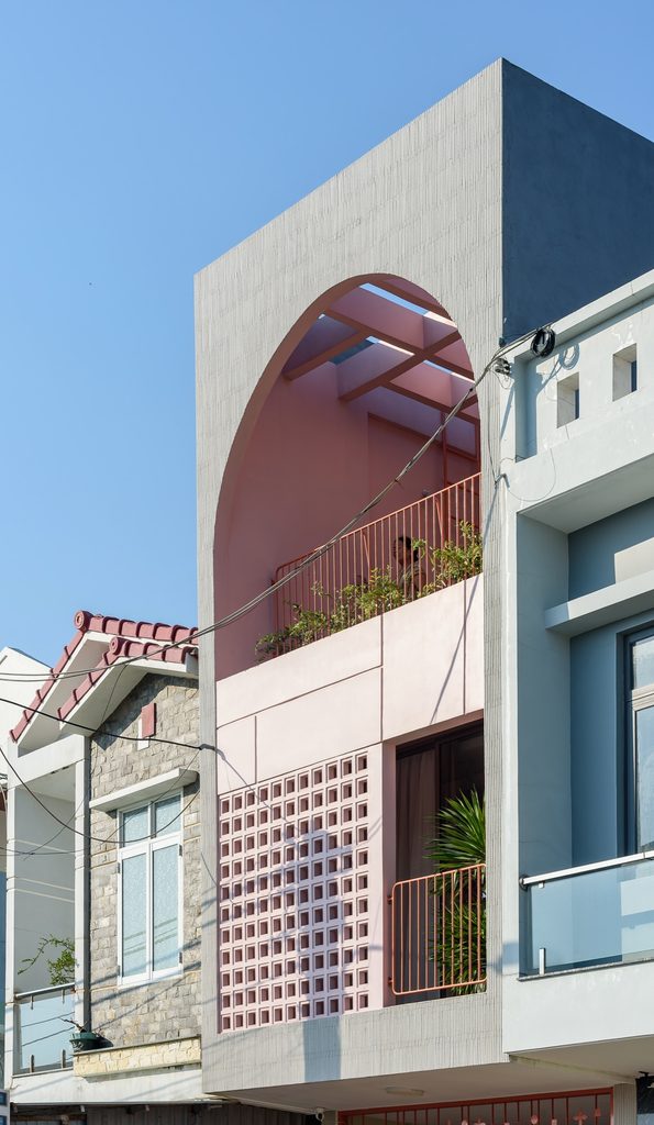 Tomi House viewed from the street, with a pink balcony and arched opening
