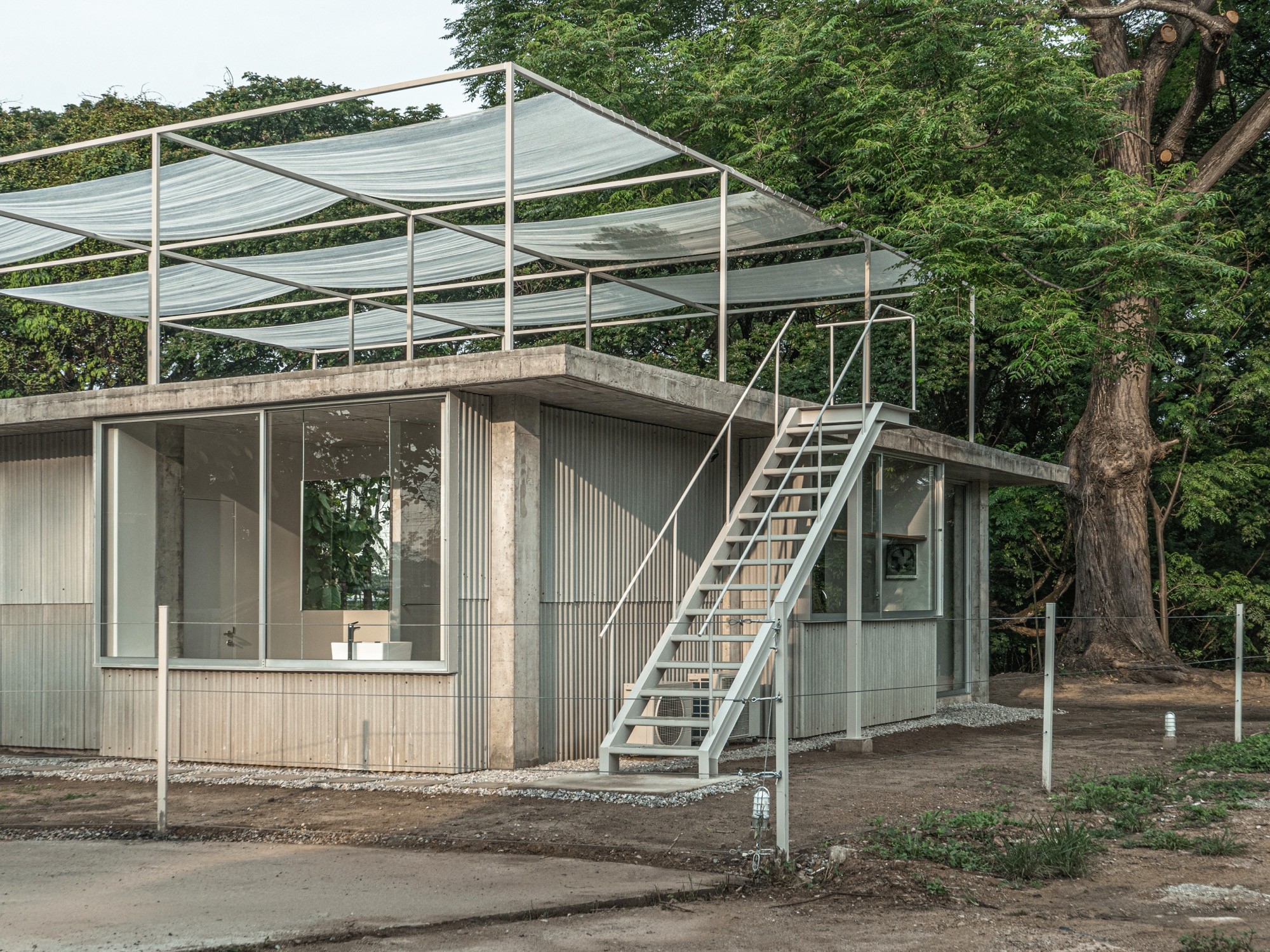 A concrete grid opens to earth, garden, and river