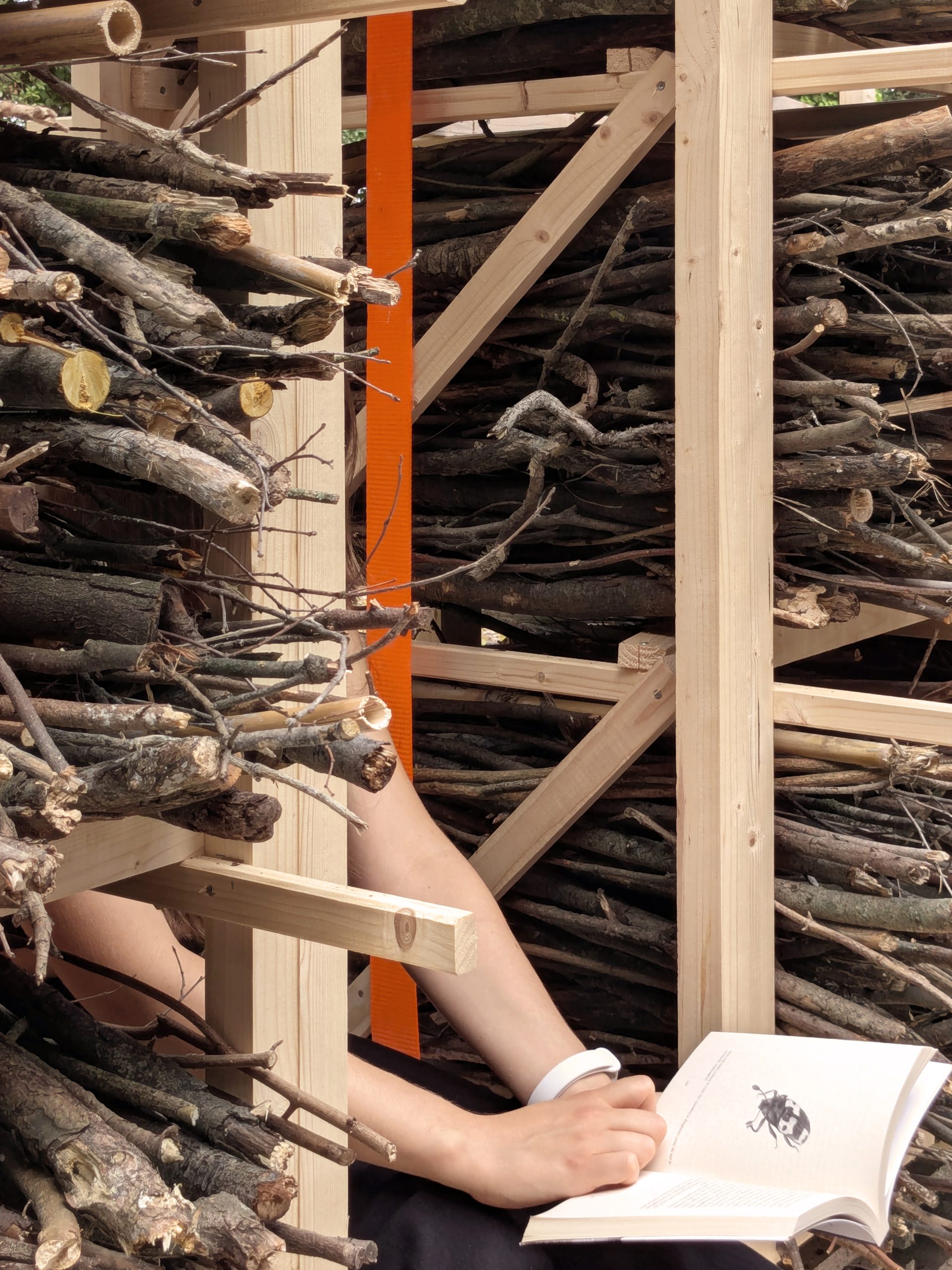 A visitor sits among the stacked branches.