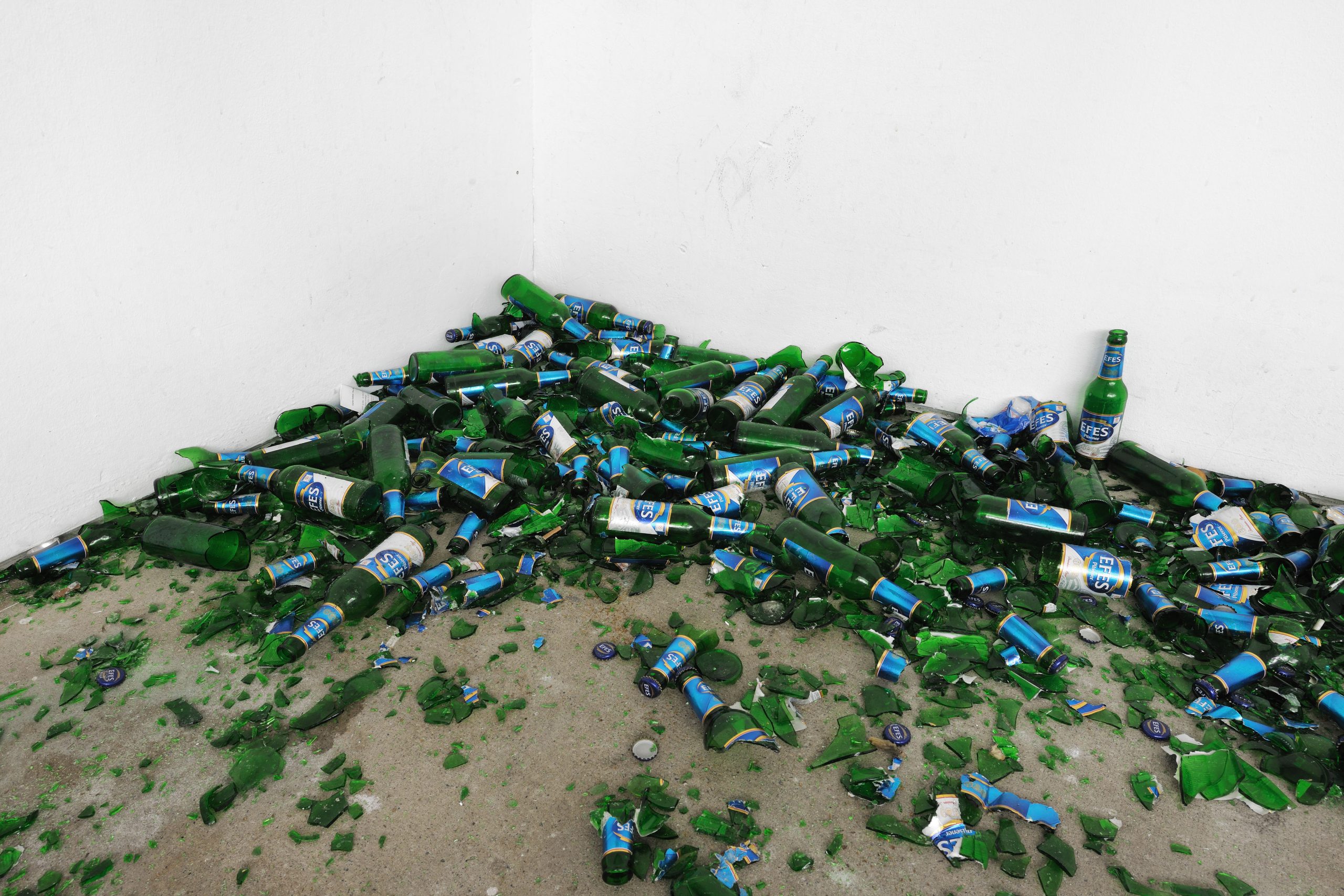 Bottles and broken glass collect in a corner.