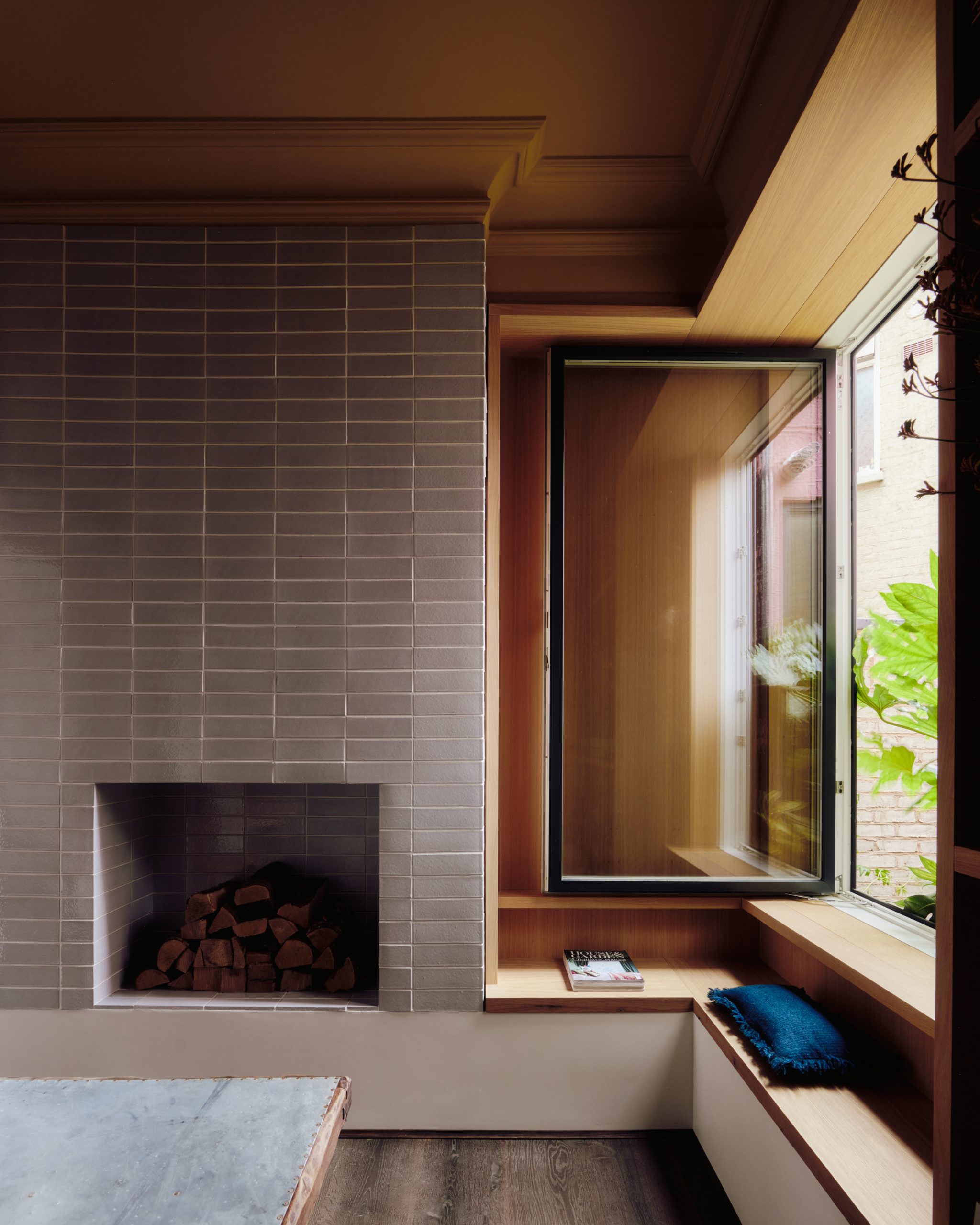 A tiled chimney breast stands beside the library window and bench.