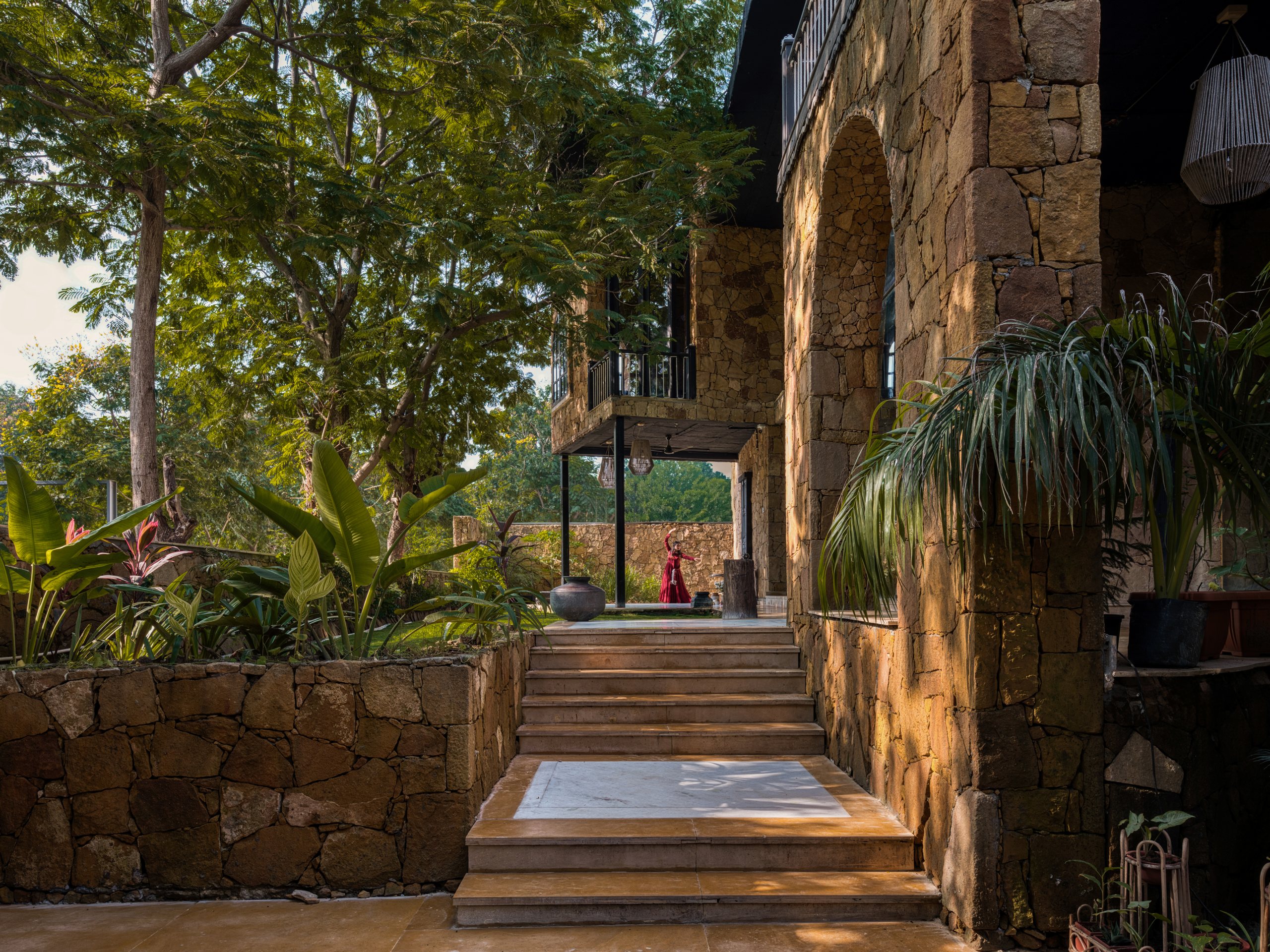 Stone steps rising beside planted terraces and arched openings at Vedalila