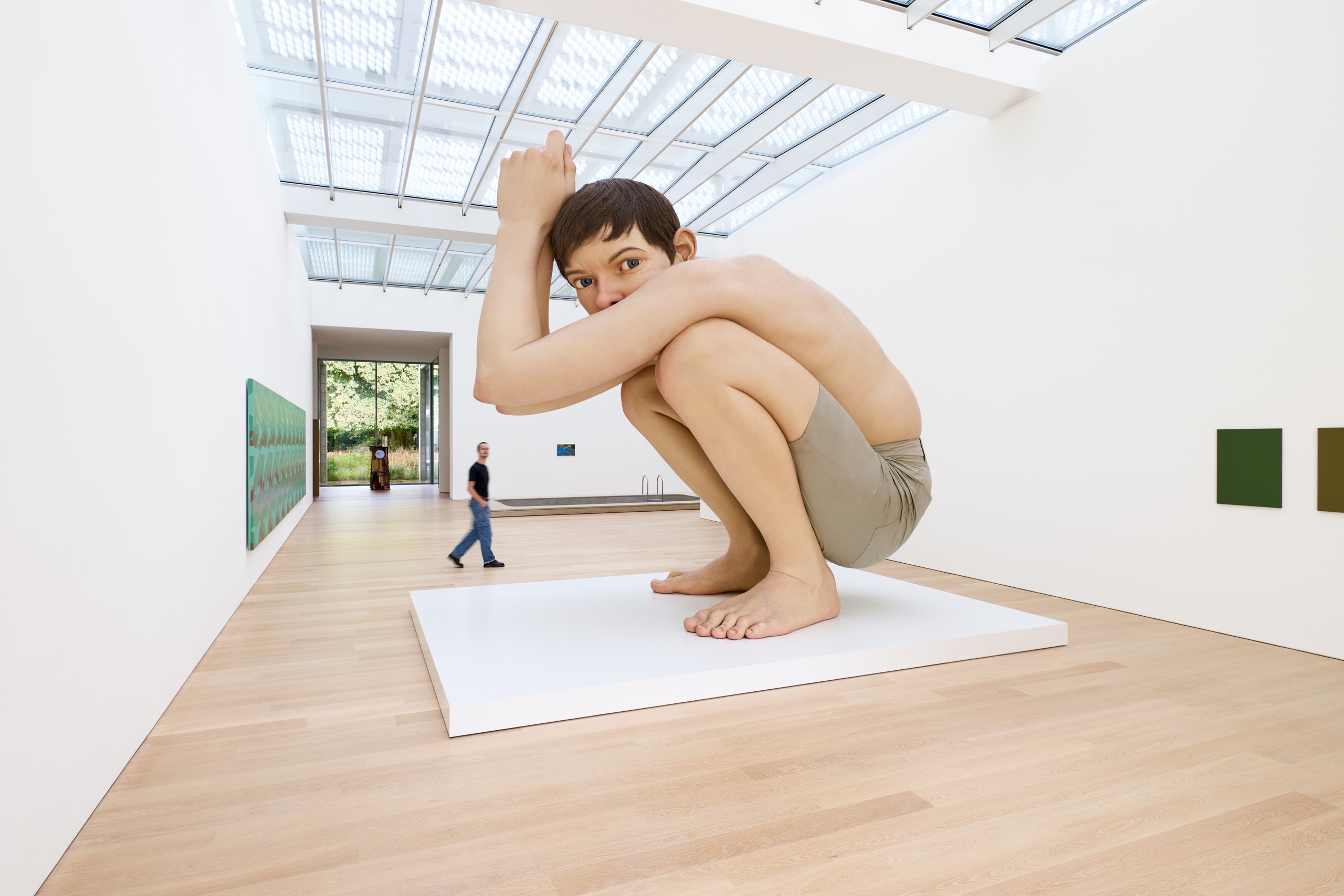 Monumental crouching figure of a boy in a light-filled museum gallery.