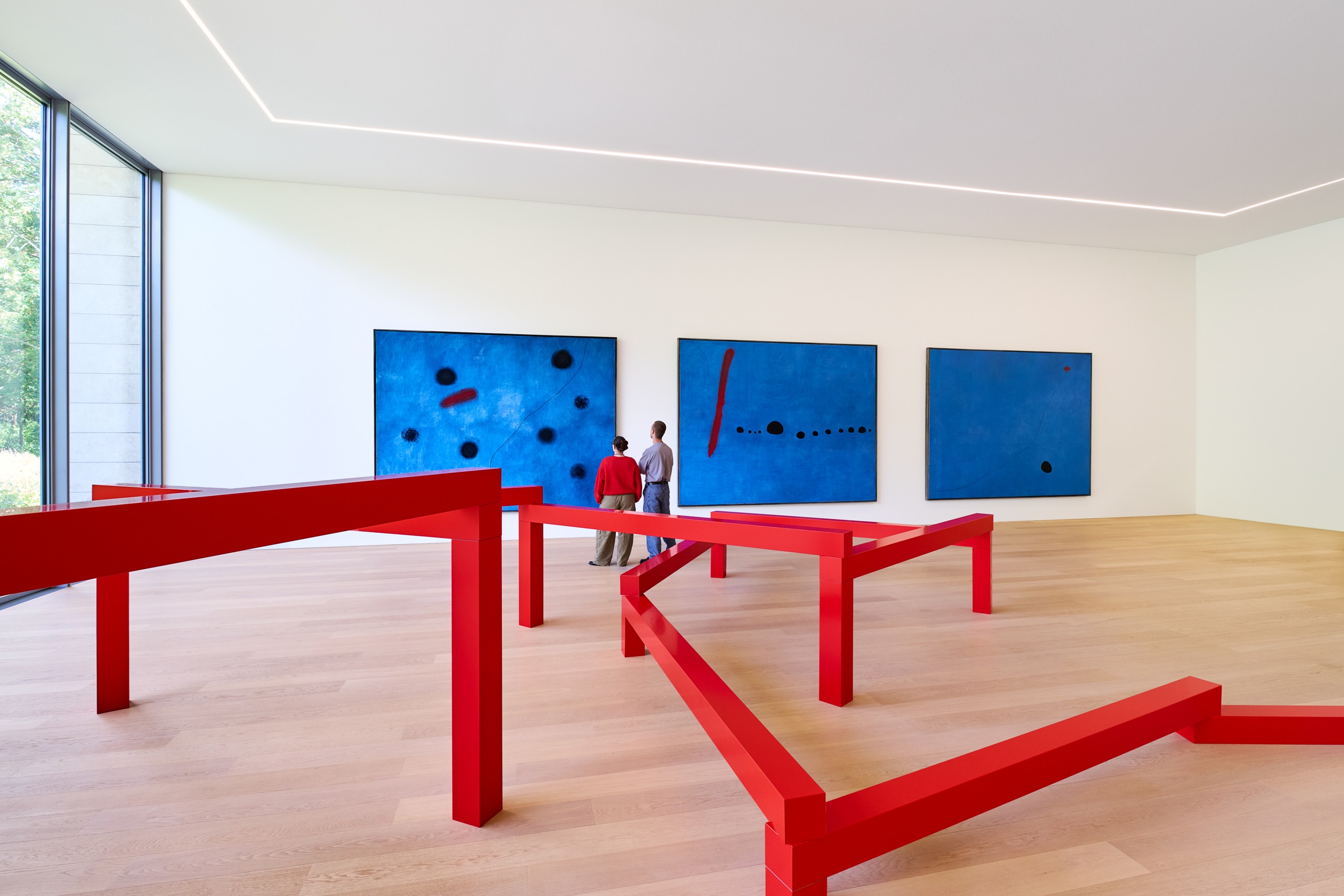 Red angular sculpture by Morellet in front of Miró’s three blue paintings.