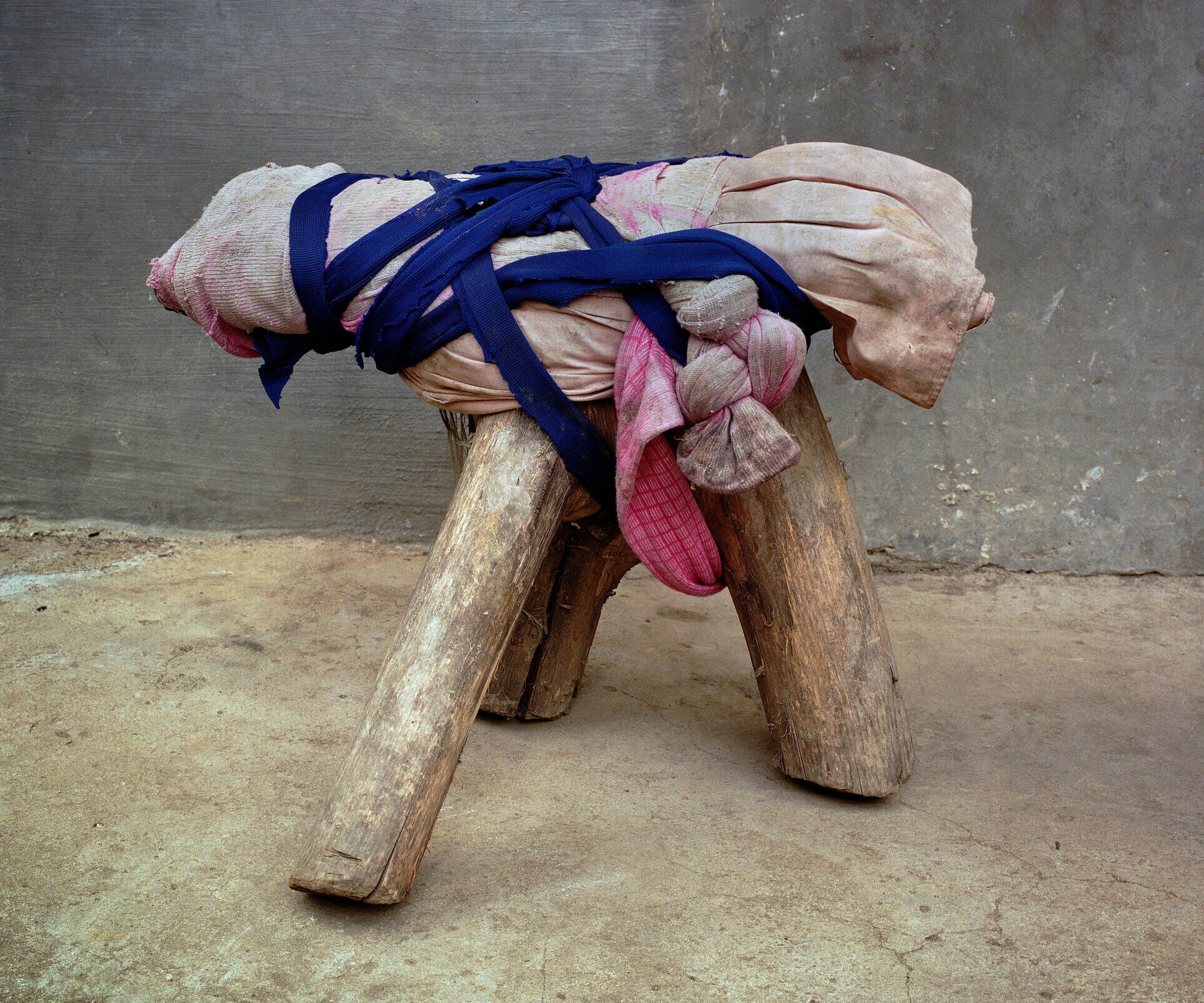 Michael Wolf, Bastard Chairs. Fabric padding is secured to a low wooden stool with blue strips.