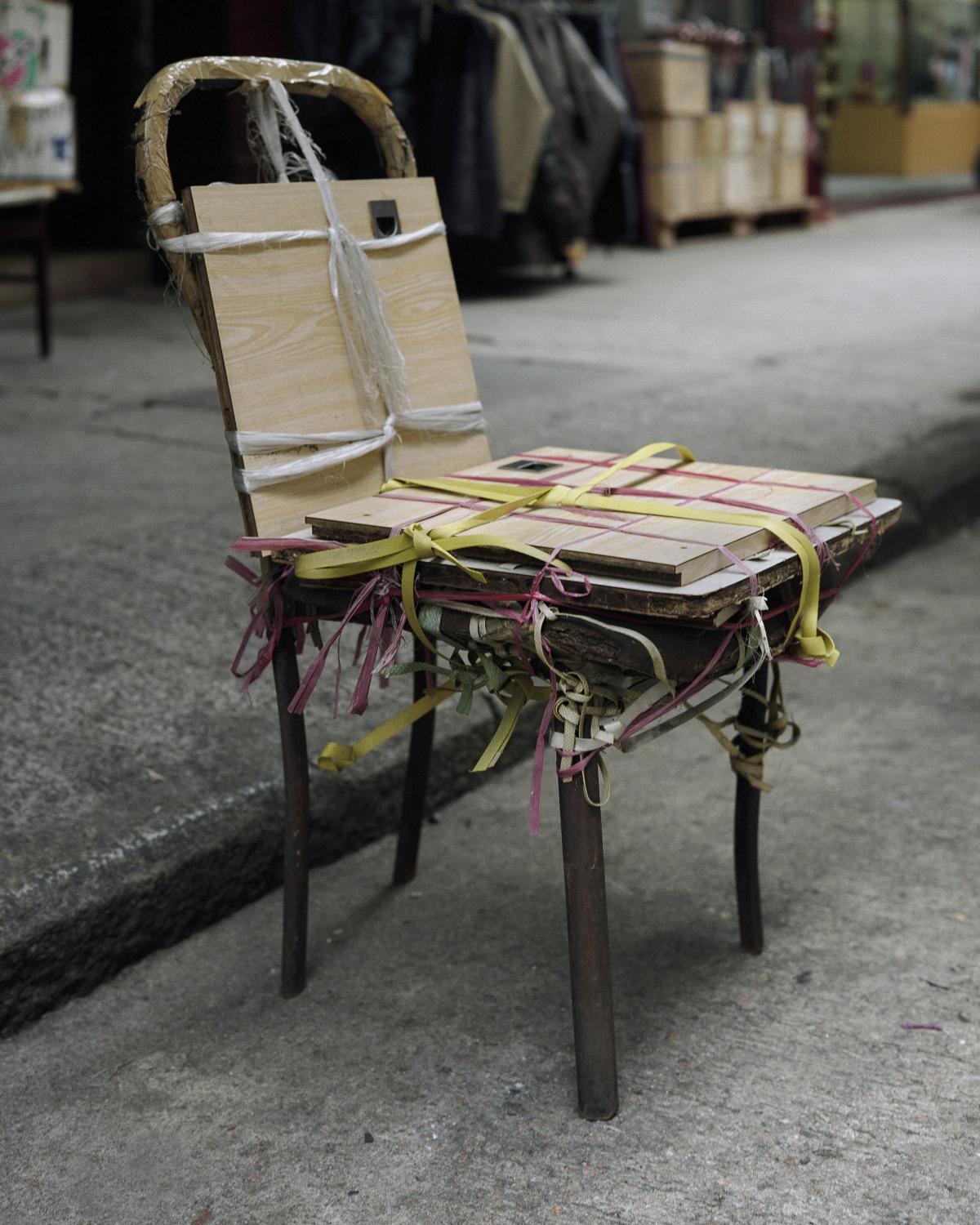 Improvised wooden chair repaired with plywood and colourful straps.