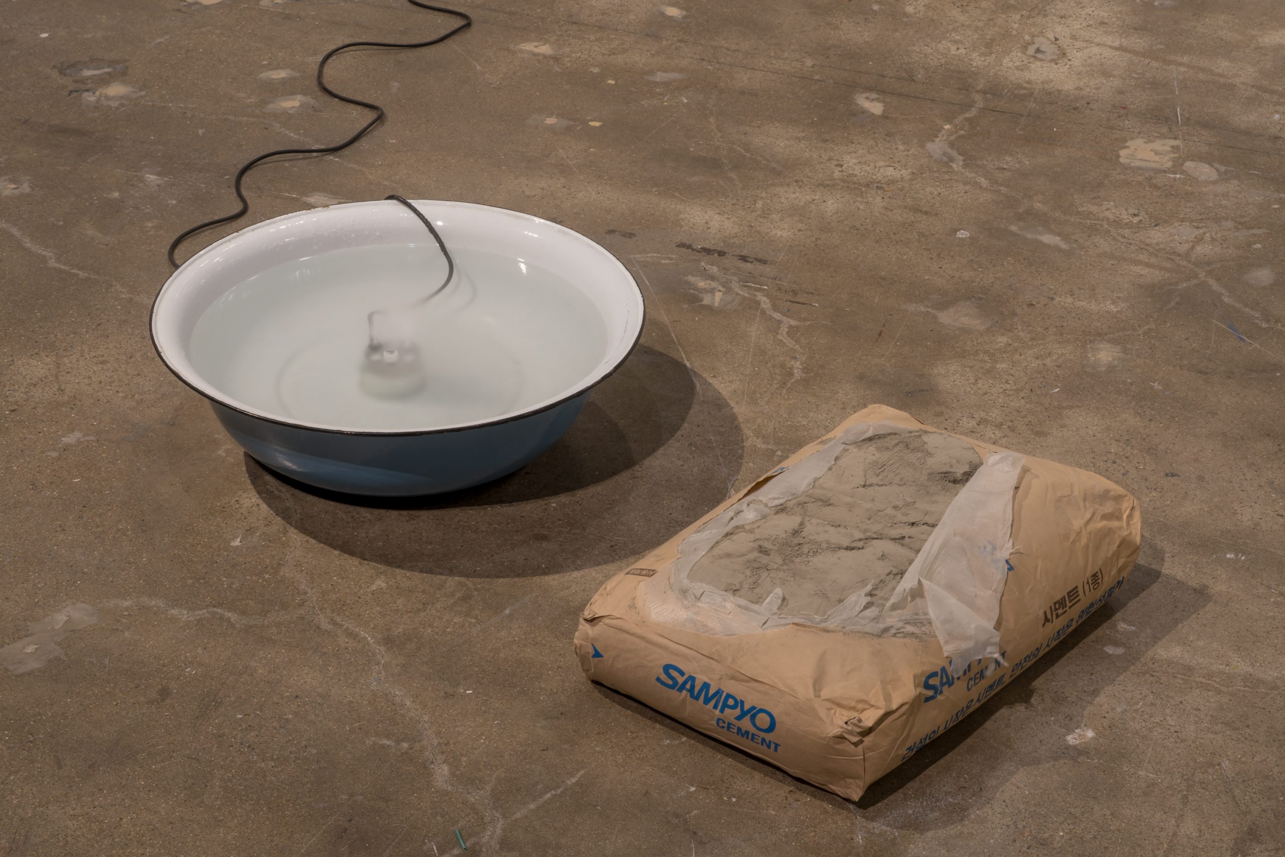 Nina Canell installation with a water-filled basin and a bag of material on the gallery floor