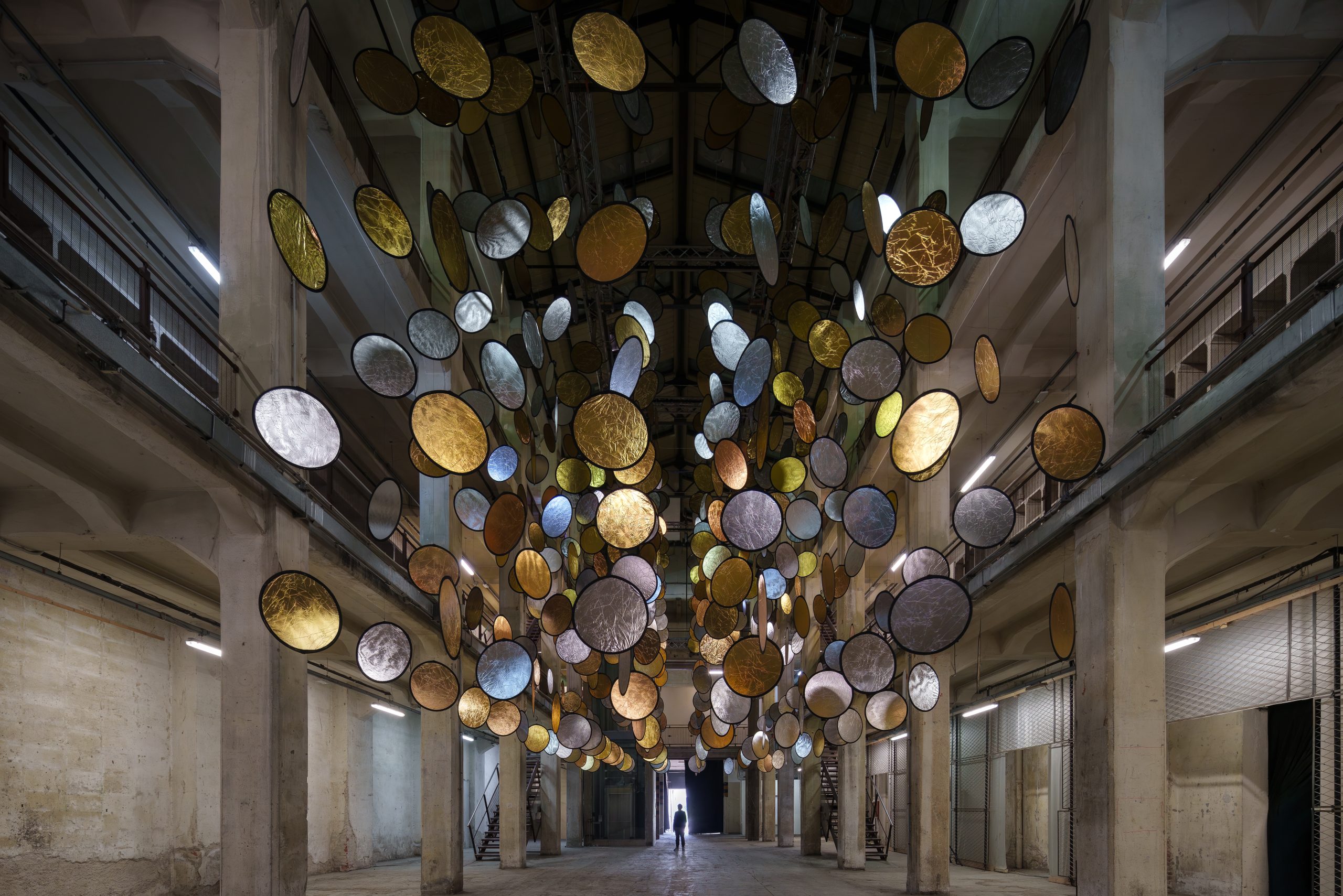 HALOS by SpY with gold and silver reflective circles suspended across a former railway factory in Florence