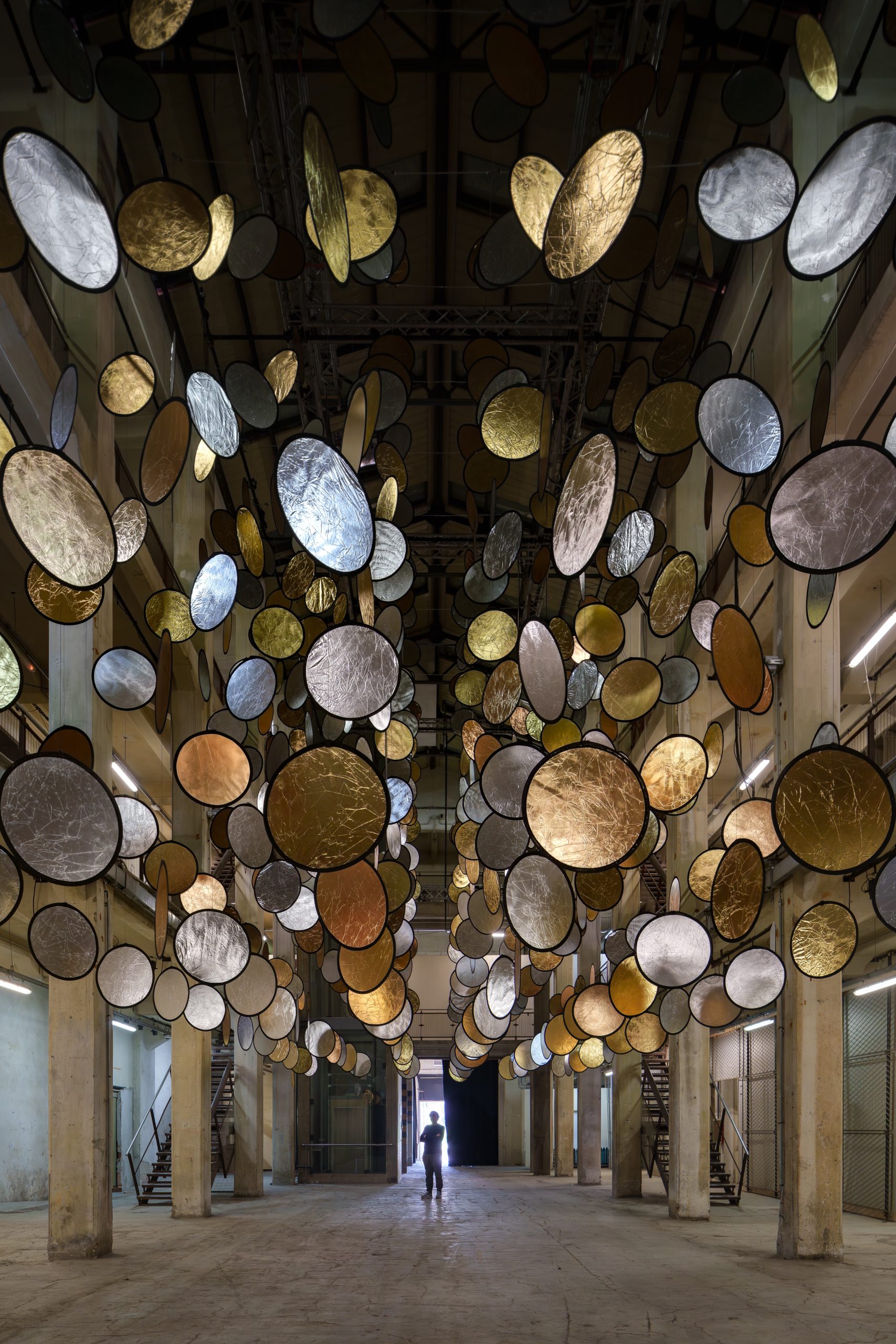 Gold and silver discs above a visitor beneath SpY's HALOS installation